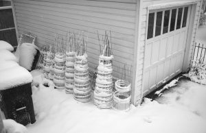 tomato cages stacked next to a garage, everything covered in snow